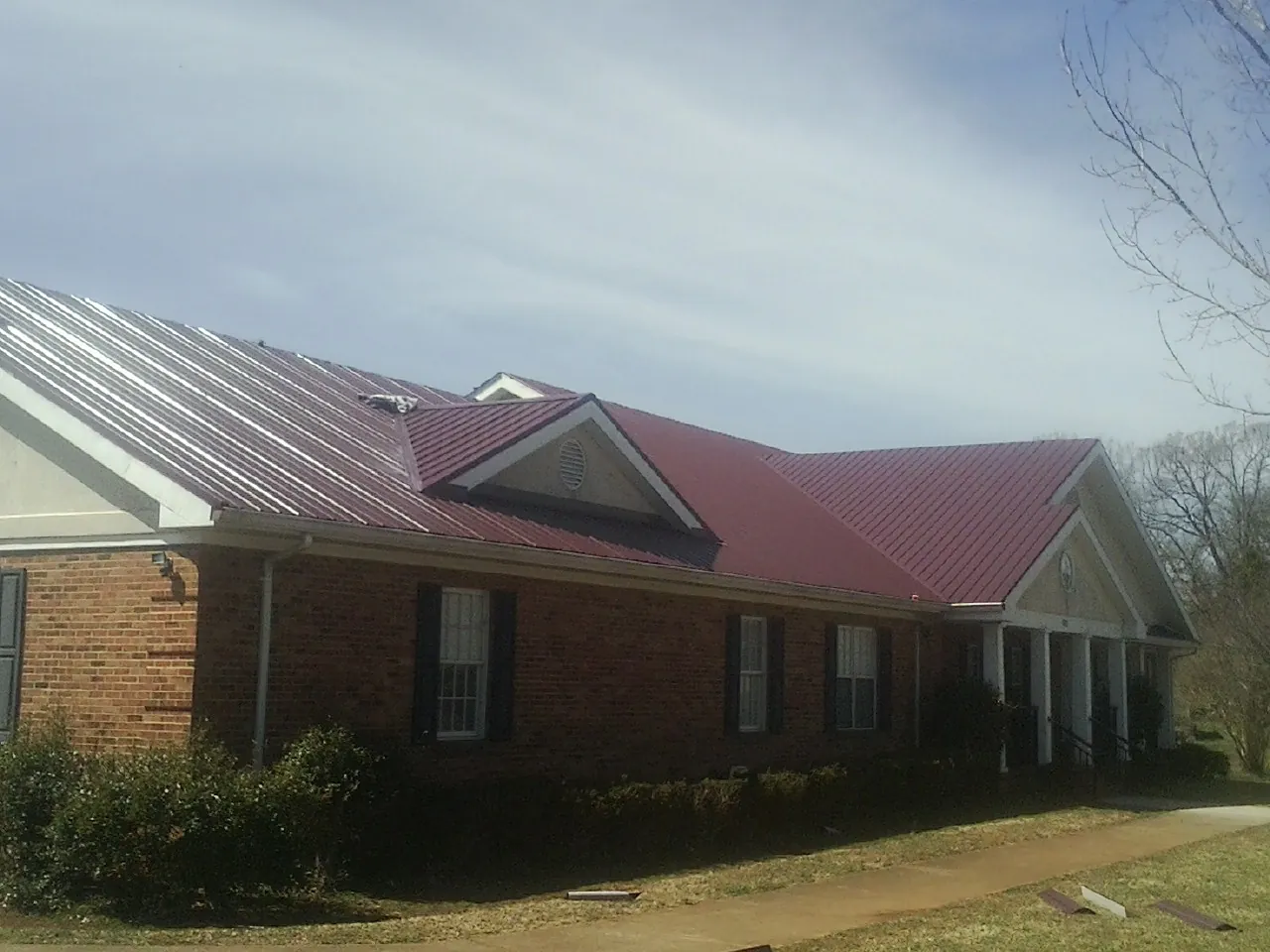 Red metal roof with gabled entries on a long brick building, from a Hail Damage Roof Repair job in Oakland City