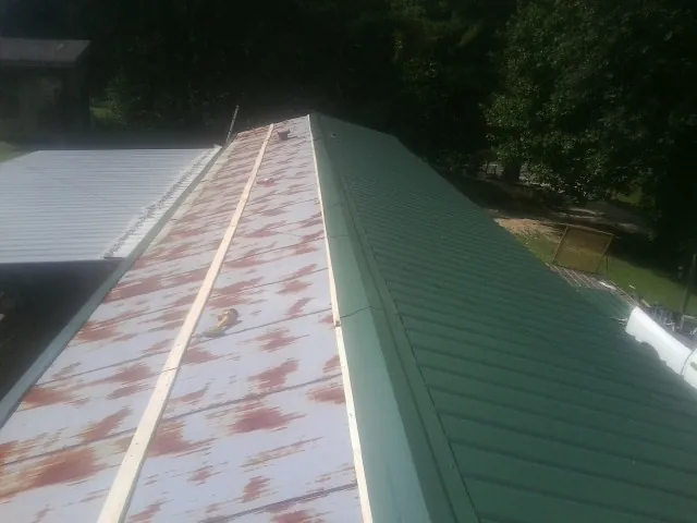 Old rusted panels beside newly installed green metal roofing — Wind Damage Roof Repair by Roofing Brothers in Oakland City