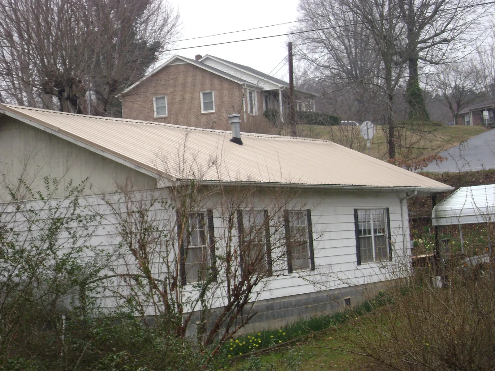 Tan metal roof on a white sided house set into a hillside — Commercial Roofing by Roofing Brothers in Oakland City